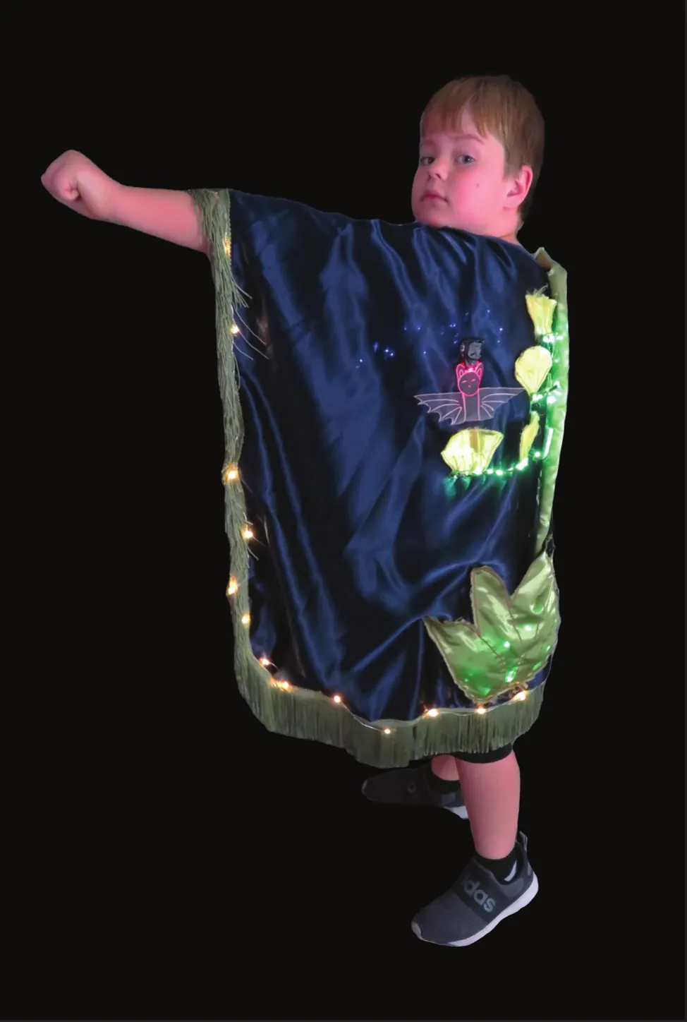 Neighbors in Harmony: student spreading a dark cape decorated with desert plants and edged in lights