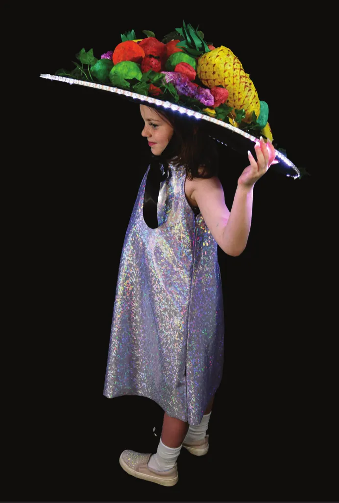 Tutti-Fruity: student in a sparkly silver dress under a wide hat of painted fruit, its brim ringed with light